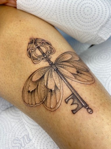 Tatuagem fineline de chave antiga com asas de borboleta