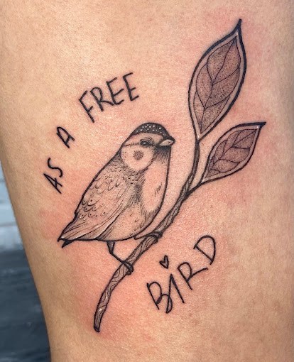 Tatuagem blackwork de pássaro em galho com a frase As a free bird